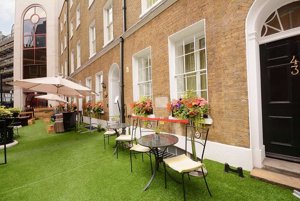 Montcalm Brewery Townhouse Ξενοδοχείο Λονδίνο Εξωτερικό φωτογραφία The photo depicts a charming outdoor area in front of a building with a warm, textured brick facade. There is a neatly maintained lawn, likely made of artificial grass, and several small round tables with chairs are arranged outside. Flower pots with